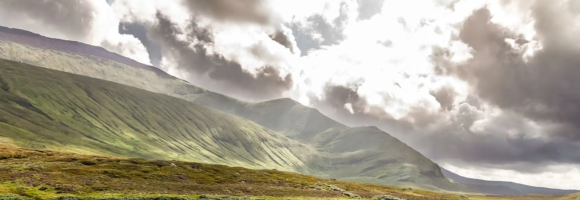Expansive view of rolling green hills and dramatic sky in the Scottish Highlands — capturing the natural beauty and origin of QSI Quality Spirits International’s premium Scotch whisky craftsmanship.
